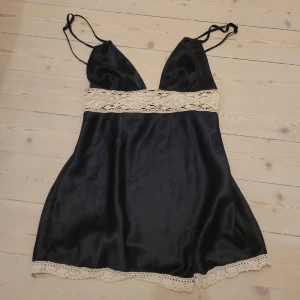Svart satin topp från Victoria's Secret - Supersöt svart topp/linne från Victoria's Secret i glansigt satinmaterial. Toppen har smala axelband, djup v-ringning och fina spetsdetaljer i beige vid midjan och nederkanten. Perfekt för dig som gillar en feminin och chic stil. Sååå fin men får inte användning för den tyvärr! Passar xxs-s🩷 knappt använd!