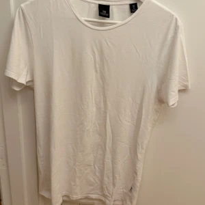 Vit t-shirt från Scotch & Soda - En stilren vit t-shirt från Scotch & Soda i mjuk bomullsblandning med lite stretch. Klassisk rund halsringning och korta ärmar. Perfekt basic-plagg med clean look och skön passform. Storlek M.