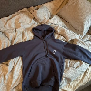 Ami Paris hoodie mörkblå - Säljer en mörkblå hoodie från Ami Paris med klassisk huva och snörning. Tröjan har en broderad Ami-logo på bröstet och en stor känguruficka framtill. Perfekt för dig som gillar stilrena och trendiga plagg. Använd ett fåtal gånger, skickar i samma påse som den kom i.