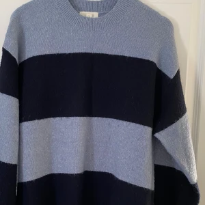 Randig stickad tröja från H&M - Mysig stickad tröja från H&M i storlek L med breda marinblå och ljusblå ränder. Tröjan har rund halsringning och långa ärmar, perfekt för kyliga dagar. Enkel och stilren design som passar till jeans eller kjol.