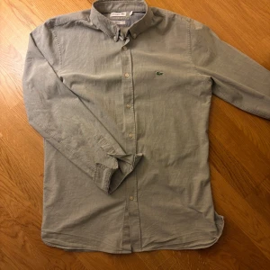 Grå skjorta från Lacoste, slim fit - En snygg grå skjorta från Lacoste. Den är slim fit och i storlek M med en broderad logga på bröstet. Hör av er om frågor uppstår. ⭐️