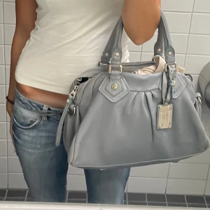 Grå handväska Marc by Marc Jacobs - Snygg grå handväska från Marc by Marc Jacobs i mjukt skinn. Väskan har dubbla handtag, silverfärgade metalldetaljer och en ikonisk metallbricka framtill. Invändigt finns ett coolt mönstrat foder och dragkedjefack med logga.  Skriv till mig privat så kan jag skicka fler bilder🥰