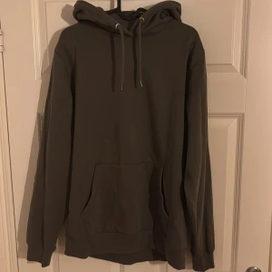 Mörkgrön hoodie - Säljer en stilren mörkgrön hoodie med huva och dragsnören. Tröjan har en stor magficka och långa ärmar, perfekt för en avslappnad look.