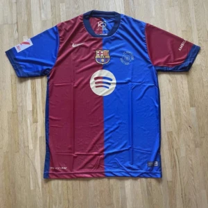 FC Barcelona Lamine Yamal matchtröja - Säljer en officiell FC Barcelona fotbollströja från Nike med Lamine Yamal och nummer 19 på ryggen. Tröjan har korta ärmar, är delad i rött och blått med klubbmärke, Spotify-logga och UNHCR-tryck. Tillverkad i lätt polyester för maximal komfort på planen.