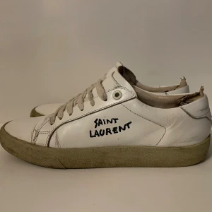 Saint Laurent skor  - Säljer ett par vita Saint Laurent sneakers med handskriven logga på sidan. Är sliten på insidan men ser ny ut på utsidan. Skriv i dm om du har frågor. Man får också låda och lite andra saker.