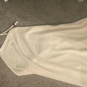 Vit omlottklänning  - Säljer en vit kort omlottklänning från Hm L. Klänningen har tunna axelband med knyt och är tillverkad i ett mjukt, frottéliknande material. Perfekt för sommarens varma dagar och har en enkel, stilren look.