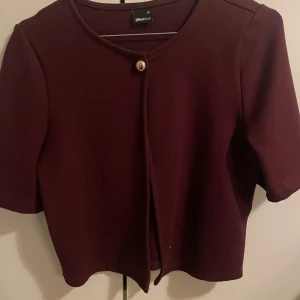 Vinröd kofta från Gina Tricot XS - Vinröd kofta från Gina Tricot i storlek XS. Kort modell med rund halsringning och en snygg guldfärgad knapp framtill. Koftan har korta ärmar och är gjord i ett mjukt stickat material. Perfekt att slänga över en topp för en stilren look. Upplevs större än xs.💕