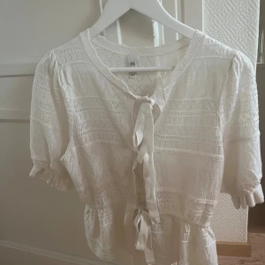 Söt vit blus med snörning från River Island - Säljer en söt vit blus från River Island med korta ärmar och volangdetaljer. Blusen har ett stickat mönster och knytband framtill. Materialet är stickad och känns mjukt mot huden. Passar som en xs-m beroende på hur man vill att den ska sitta.