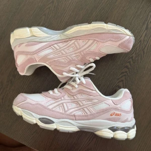 ASICS sneakers i ljusrosa och vitt - Snygga ASICS sneakers i ljusrosa och vitt med meshpaneler och detaljer i mocka. Skorna har en chunky vit sula med grå inslag och klassisk snörning. Perfekt för dig som gillar sportig stil och vill ha bekväma skor med cool design.