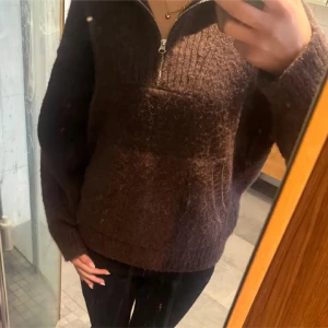 Brun stickad tröja med half zip - Mysig brun stickad tröja med half zip framtill och ribbad detalj vid halsen. Tröjan har långärmade och en loose passform som gör den perfekt för kyliga dagar. Passar dig som gillar avslappnad stil och vill ha något varmt och skönt.