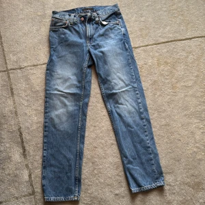 Gritty Jackson jeans från Nudie Jeans - Klassiska blå jeans från Nudie Jeans med raka ben och snygga slitningar. Jeansen har fem fickor, orange kontrastsömmar och Nudie-logga på bakfickan. Tillverkade i bomull med dragkedja och knapp framtill.