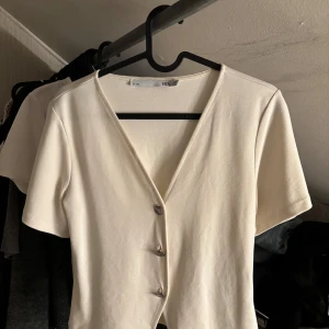 Vit kortärmad blus från lager 157 - Säljer en vit blus från 157 i storlek XS. Toppen har korta ärmar, v-ringning och tre silver knappar framtill. Perfekt för dig som gillar en enkel men trendig look. Materialet känns mjukt och skönt mot huden. 