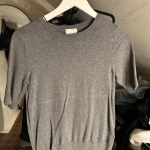 Grå kortärmad tröja från H&M - En grå tröja från H&M i storlek XS. Tröjan har korta ärmar, rund halsringning och är tillverkad i mjukt material. 