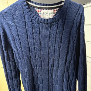 Mörkblå stickad tröja från Bondelid - Säljer en mörkblå stickad tröja från Bondelid i klassisk kabelstickad design.Passar även storlek M Tröjan har rund halsringning, långa ärmar och en snygg läderdetalj med logga vid nederkanten. Perfekt för kyliga dagar och enkel att matcha med jeans. Passar inte mig därför jag säljer