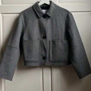 Grå croppad rock från Zara - Grå kappa från Zara med klassisk krage och stora framfickor. Jackan har en stilren look med raka linjer, knäppning med svarta knappar och långärmade ärmar. Använd få gånger. Storlek 152💗