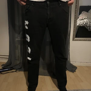 Svarta Dsquared2 ICON jeans med tryck - Svarta jeans från Dsquared2 med stort vitt 'ICON' tryck och Dsquared2-logga längs ena benet. Klassisk femficksmodell med raka ben och normal passform. Jeansen har tydlig streetkänsla och är tillverkade i bomull med snygga detaljer.