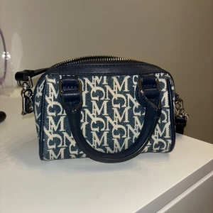 Mango väska  - Snygg liten handväska från Mango i blått och vitt med tydligt monogrammönster. Väskan har två handtag, avtagbar axelrem och dragkedja upptill. Materialet är en mix av textil och skinn, perfekt för dig som gillar statement-accessoarer.