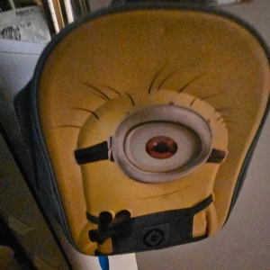 Minions ryggsäck med tryck - Rolig ryggsäck med stort Minions-motiv på framsidan. Väskan är gul och blå med ett stort öga och detaljer från filmen. Justerbara axelband och dragkedja upptill. Perfekt för dig som älskar Minions och vill sticka ut i skolan eller på stan.