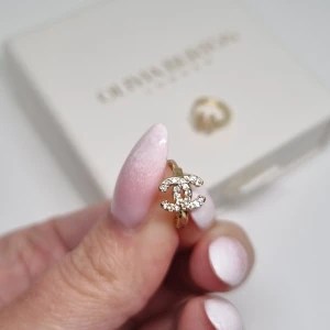 Cc örhängen i guld med strass - Supersnyggal örhängen i guld med klassiska CC-loggan täckt av glittrande strass. Små och eleganta hoops som ger en lyxig vibe och passar perfekt till din outfit. Ikonisk design som verkligen sticker ut och känns exklusiv.