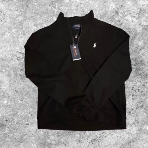 Svart half zip tröja Polo Ralph Lauren - Svart långärmad tröja från Polo Ralph Lauren känns som S med half zip och klassisk broderad logga på bröstet. Tröjan har en hög krage och är i bomull, perfekt för en clean och stilren look. Custom fit-modell som sitter snyggt utan att vara för tight.