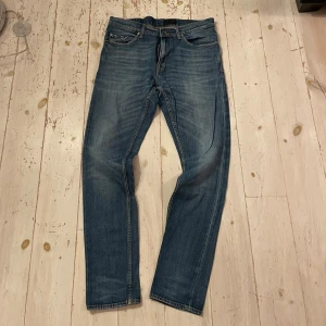Tiger of Sweden Blå jeans modell Pistolero 32/32  - Snygga blå jeansbyxor från Pistolero i klassisk tvätt med lätt slitning. Modellen har raka ben, fem fickor och orangea sömmar. Perfekta för dig som gillar en tidlös och avslappnad look. Tillverkade i jeansmaterial och passar till många olika stilar.