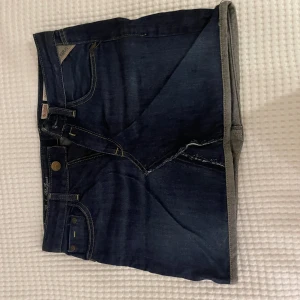 Mörkblå jeanskjol från Replay - Snygg mörkblå jeanskjol från Replay med klassiska fickor fram och bak, samt detaljerade sömmar. Kjolen har rå kant nertill och stängs med dragkedja och knapp. Perfekt för dig som gillar en avslappnad och cool stil. Använd fåtal gånger och inget som syns, köpta för 2500kr