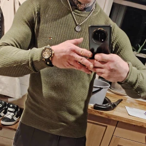 TOMMY HILFIGER Knitwear olivfärgad stickad tröja [M]  - Snygg olivgrön stickad slimfit tröja från Tommy Hilfiger med diskret logga på bröstet. Tröjan har rund halsringning, ribbade muddar och lång ärm. Perfekt för lager-på-lager och passar till både jeans och träningsbyxor.