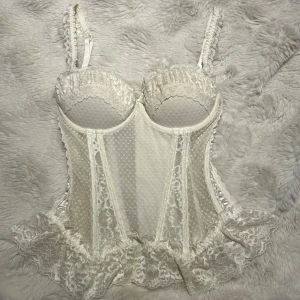 Vit spetskorsett från H&M - Superfin vit korsett från H&M med spetsdetaljer, volangkant och prickigt mönster. Justerbara axelband(kan tas av) med spets och hakknäppning bak. Materialmix av satin och spets ger en lyxig känsla. Perfekt för dig som vill ha något extra till outfiten.