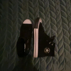 Svarta Converse Chuck Taylor high - Klassiska svarta Converse Chuck Taylor All Star high-top sneakers med vit tå och sula. Skorna har snörning, rund tå och tydlig Converse-logga på sidan. Tillverkade i canvas med gummisula och vita detaljer längs sulan.