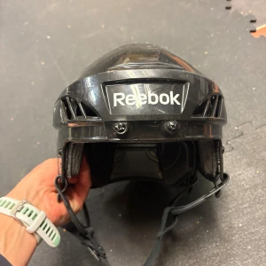 Svart hockeyhjälm Reebok - Säljer en svart hockeyhjälm från Reebok. Hjälmen har justerbar passform, vadderad insida och hakrem . Passar perfekt för dig som vill åka skridskor. Tror att storleken är 3 K passar ett barn runt 5-12 år. Kan föröka mäta insidan om intresse finns. 
