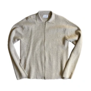 Beige full zip tröja från Sandö - Snygg beige kofta från Sandö i mjukt material. Koftan har hel dragkedja framtill, klassisk krage och långa ärmar. Perfekt för lager-på-lager och ger en clean look till din outfit.