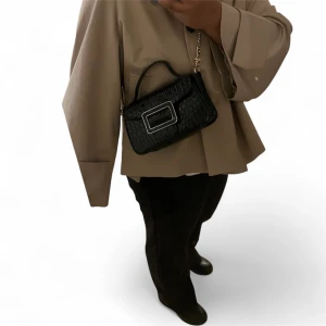 Zara axelväska med krokoprägling - svart - Snygg svart axelväska med krokopräglat mönster och en stor guldfärgad spännesdetalj framtill. Väskan har både handtag och kedjerem, vilket gör den enkel att bära på olika sätt. Perfekt accessoar för att lyfta din outfit.