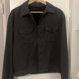 Svart overshirt från Contemporary - Stilren svart overshirt från Contemporary i storlek L. Jackan har klassisk krage, två bröstfickor med knappar och raka ärmar. Perfekt för lager-på-lager och enkel att matcha med olika outfits. 