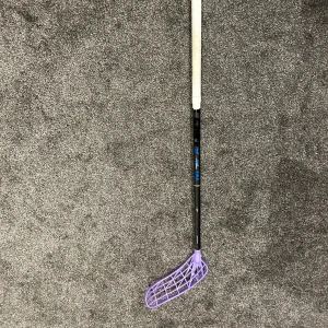 Unihoc unislim max - Bilderna visar en innebandyklubba med svart skaft, vit grepptejp och ett lila blad. Produkten verkar vara i gott skick utan synligt slitage eller defekter. Perfekt för både träning och matchspel. Märke och modell är inte identifierbara från bilderna.