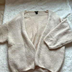 Beige stickad kofta från Lindex - Mysig och oversized beige stickad kofta från Lindex. Koftan har en öppen front utan knappar, lång ärm och en mjuk, fluffig känsla. Perfekt att slänga på sig över en t-shirt eller topp för extra värme.