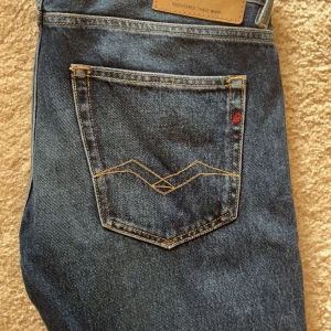 Blå Replay jeans straight fit - Säljer ett par klassiska blå jeans från Replay med snygga kontrastsömmar och logga på fickan. Jeansen har rak passform och normal midja, tillverkade i slitstarkt denim. Perfekta för dig som gillar en tidlös och clean look.