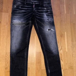 Svarta Dsquared2 jeans med slitningar NYA - Säljer ett par svarta jeans från Dsquared2 med coola slitningar och blekta detaljer på låren. Jeansen har en klassisk femficksmodell och är tillverkade i jeansmaterial. Snyggt smal passform och diskreta färgskiftningar för en trendig look.