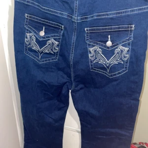 Blå jeans med broderade bakfickor - Snygga blå jeans med kontrasterande vita sömmar och broderade detaljer på bakfickorna. Köpt på second hand i Tyskland å står ingen exakt storlek men passar om man har midjemått mellan 85-90 cm. De är högmidjade