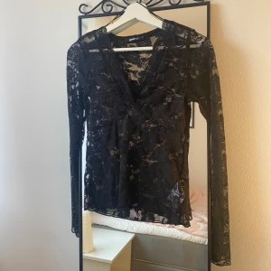 Svart spetsblus spetstopp festopp - Supersnygg svart topp i transparent spets från Gina Tricot. Blusen har långärmade ärmar, v-ringad hals och ett blommigt spetsmönster över hela plagget. Perfekt för fest. 