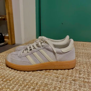 Adidas Spezial sneakers i ljusgrå mocka - Säljer ett par Adidas Spezial sneakers i ljusgrå mocka med vita detaljer och klassiska tre ränder på sidan. Skorna har vit snörning, vit hälkappa och en snygg gummisula i brunt. Fint skick! Inte använda mycket!