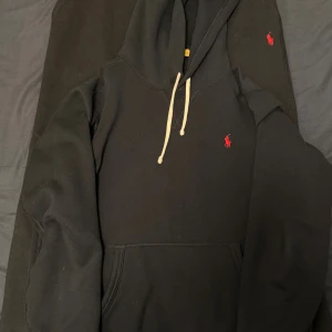 Svart set från Polo Ralph Lauren - Svart hoodie från Polo Ralph Lauren med klassisk röd broderad logga på bröstet. Tröjan har huva med vita snören och en stor magficka. Mjuk insida och långärmad modell, perfekt för chill dagar eller när du vill ha en clean streetstyle.