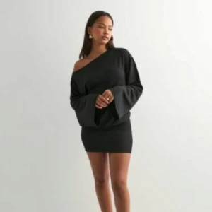 Svart offshoulder kortklänning - Snygg svart kortklänning med offshoulder och vida ärmar. Klänningen har en tight passform och är perfekt för dig som gillar en stilren look med lite edge. Enkel att styla med smycken och klackar.