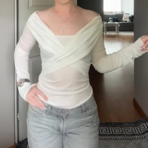 Vit omlott topp med offshoulder - Säljer en vit omlott topp med offshoulder och långa ärmar. Toppen är figurnära och har en snygg omlott-detalj framtill som ger en cool och trendig look. Perfekt att styla med jeans eller kjol för en fräsch outfit.