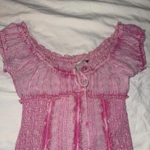 Top Urban Outfitters  - Supersöt rosa blus från Kimchi Blue fr Urban med broderade små blommor, volangdetaljer och knytning vid bysten. Blusen har korta puffärmar, smockad midja.