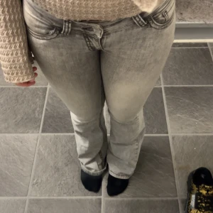 Grå bootcut jeans från Replay - Säljer ett par gråa jeans från Replay med bootcut passform och snygga detaljer på bakfickorna. Jeansen har klassisk femficksdesign, dragkedja och knapp framtill. Materialet är jeans med en tvättad look som ger en cool vibe.
