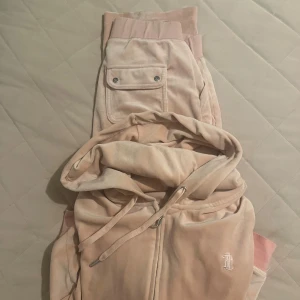 Ljusrosa Juicy Couture hoodie - Supermjuk ljusrosa hoodie från Juicy Couture i velour med dragkedja och huva. Klassisk JC-logga broderad framtill och snörning i huvan. Perfekt för chill dagar och snygg att matcha med mjukisbyxor.