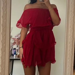 Röd offshoulder volangklänning - PLT- röd kortklänning med offshoulder och volangdetaljer. Klänningen har en luftig och flowy känsla med flera lager och elastisk midja.