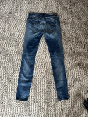 Replay Anbass skinny jeans blå - Säljer ett par Replay Anbass jeans i blå tvätt med snygga slitningar och klassiska fem fickor. Modellen är skinny med låg midja och smal passform. Jeansen har detaljerade sömmar på bakfickorna och är gjorda i stretchig bomull för extra komfort.