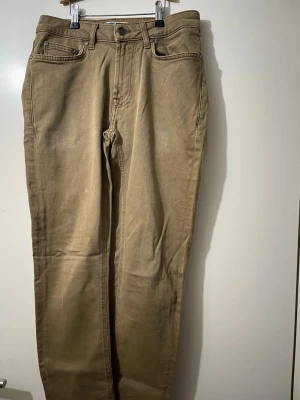 Beige raka jeans från Dressmann - Snygga beige jeans från Dressmann med klassisk femficksdesign och raka ben. Byxorna har normal passform och är tillverkade i slitstark bomull. Perfekt för dig som gillar enkel och stilren look. Färgtonen är varm och neutral, passar till det mesta.