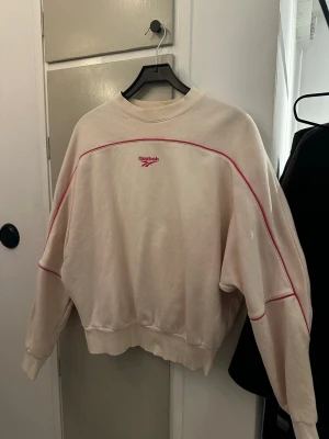Reebok vintage sweatshirt - Säljer en vintage sweatshirt från Reebok Classic med rosa logga och linjer på både fram- och baksida. Tröjan har rund hals, ribbade muddar och är långärmad. Materialet är mjuk bomull, perfekt för chill dagar.